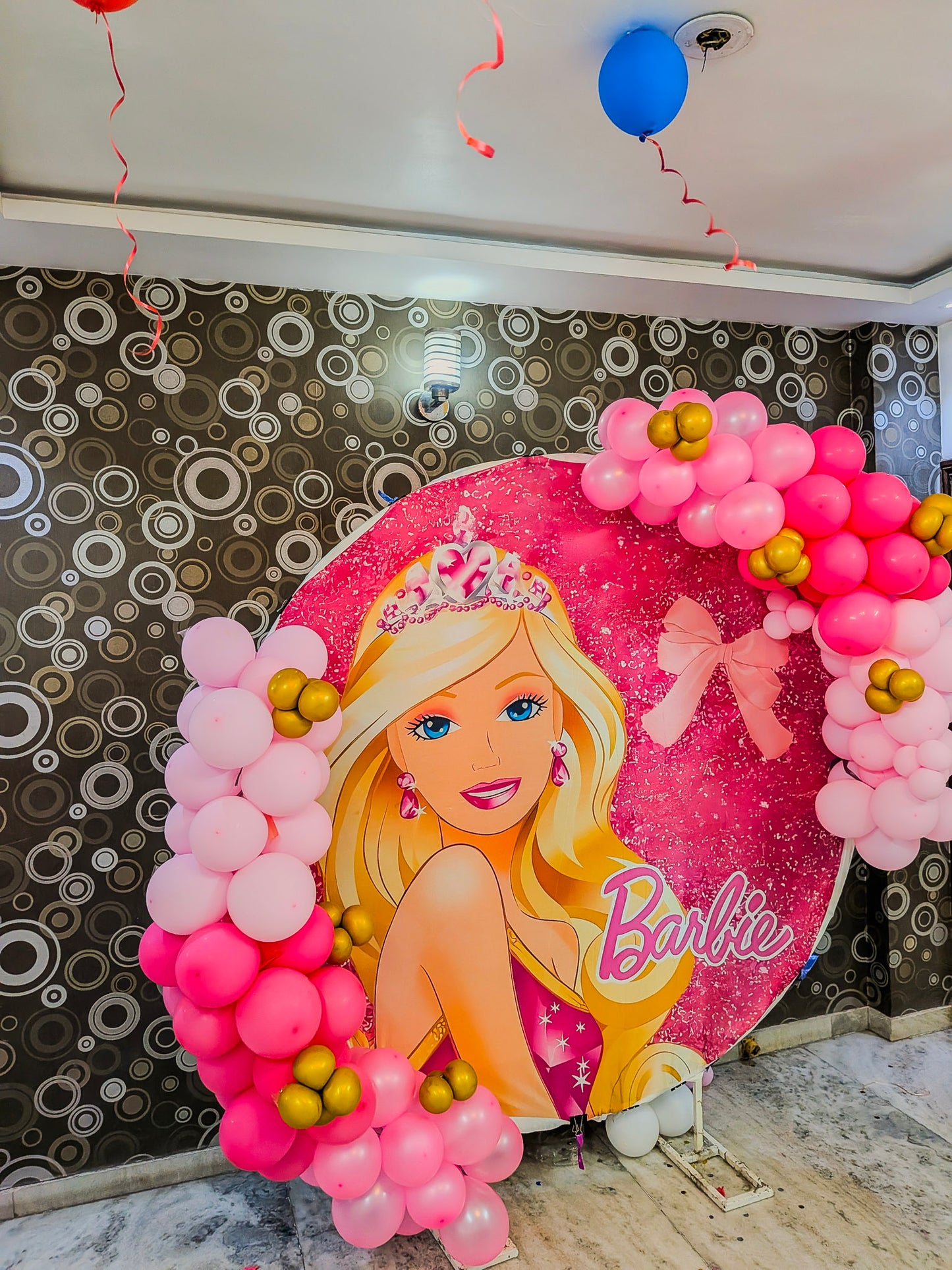 Barbie-themed balloon arch with pink and gold balloons against a decorative wall.