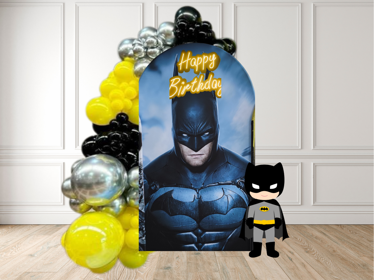 Batman-themed birthday banner with balloons and a small Batman figure on a wooden floor.