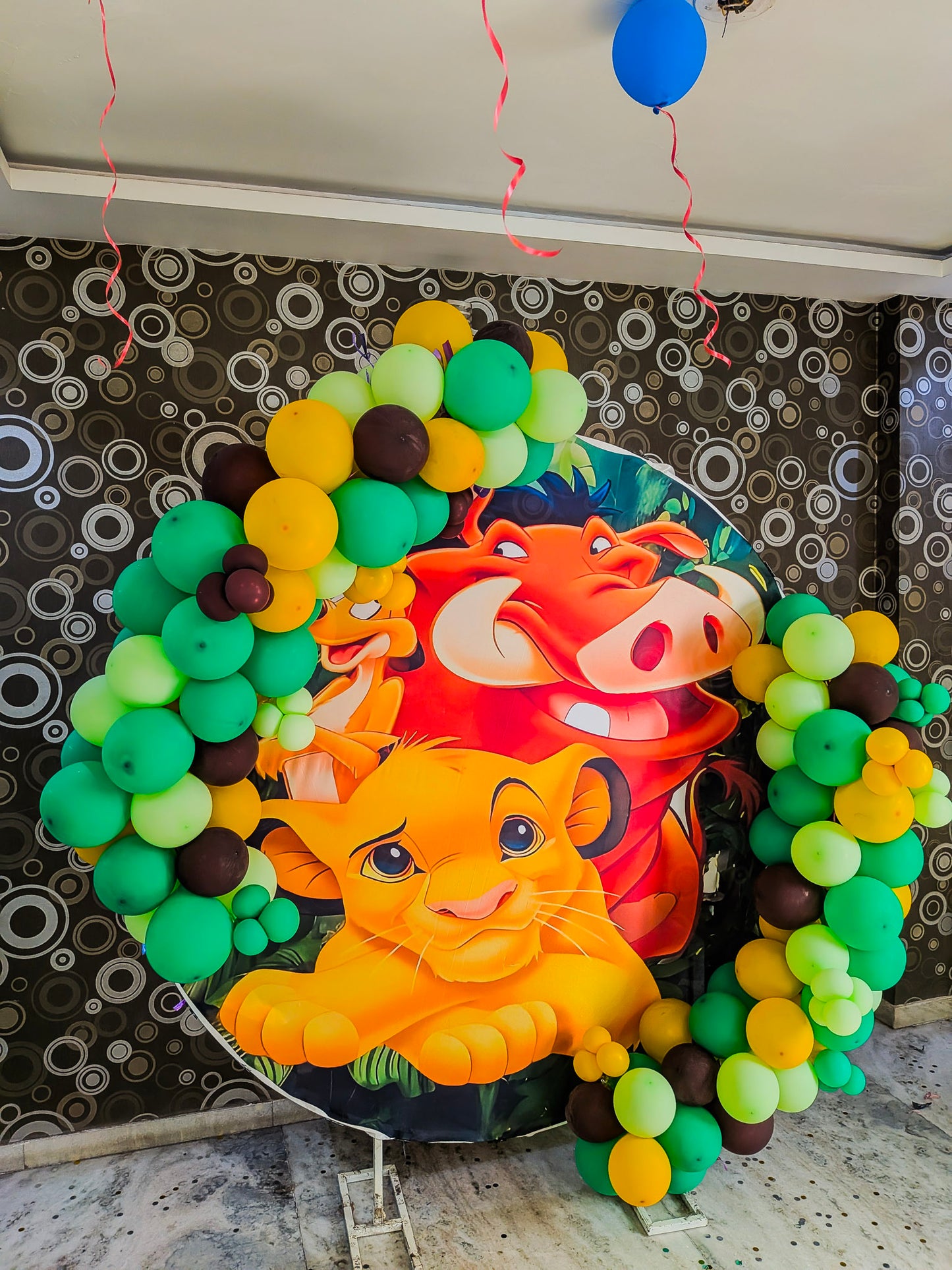 Decorative balloon arch with cartoon characters Lion King and balloons in front of a patterned wall.