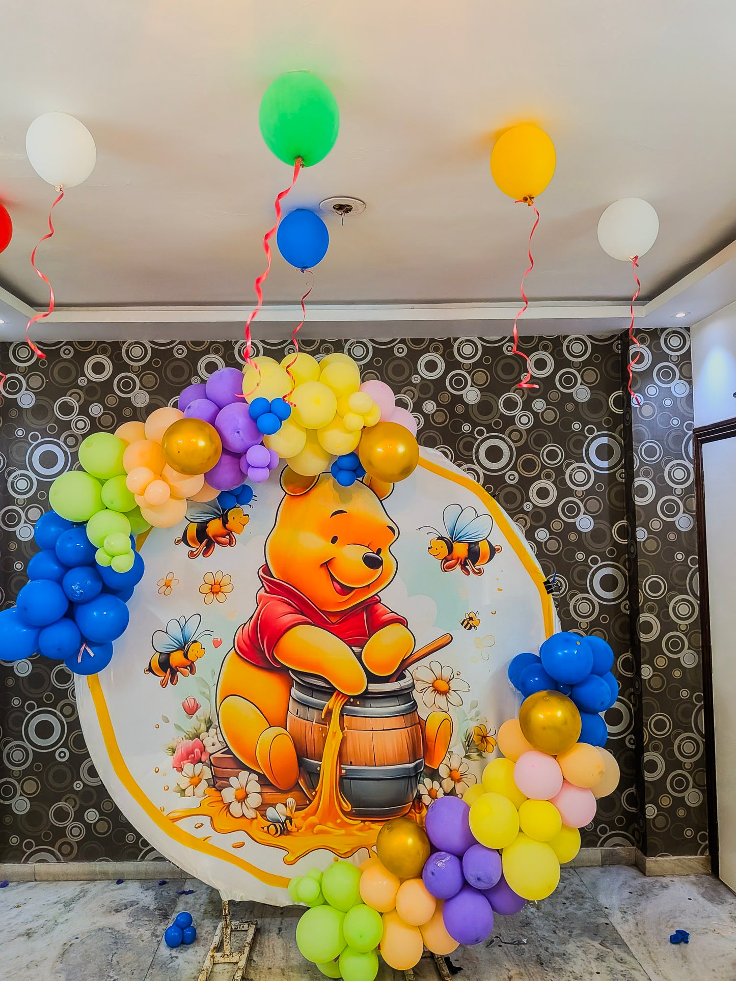 Decorative setup with balloons shaped like Winnie the Pooh and balloons in front of a wall with circular patterns.
