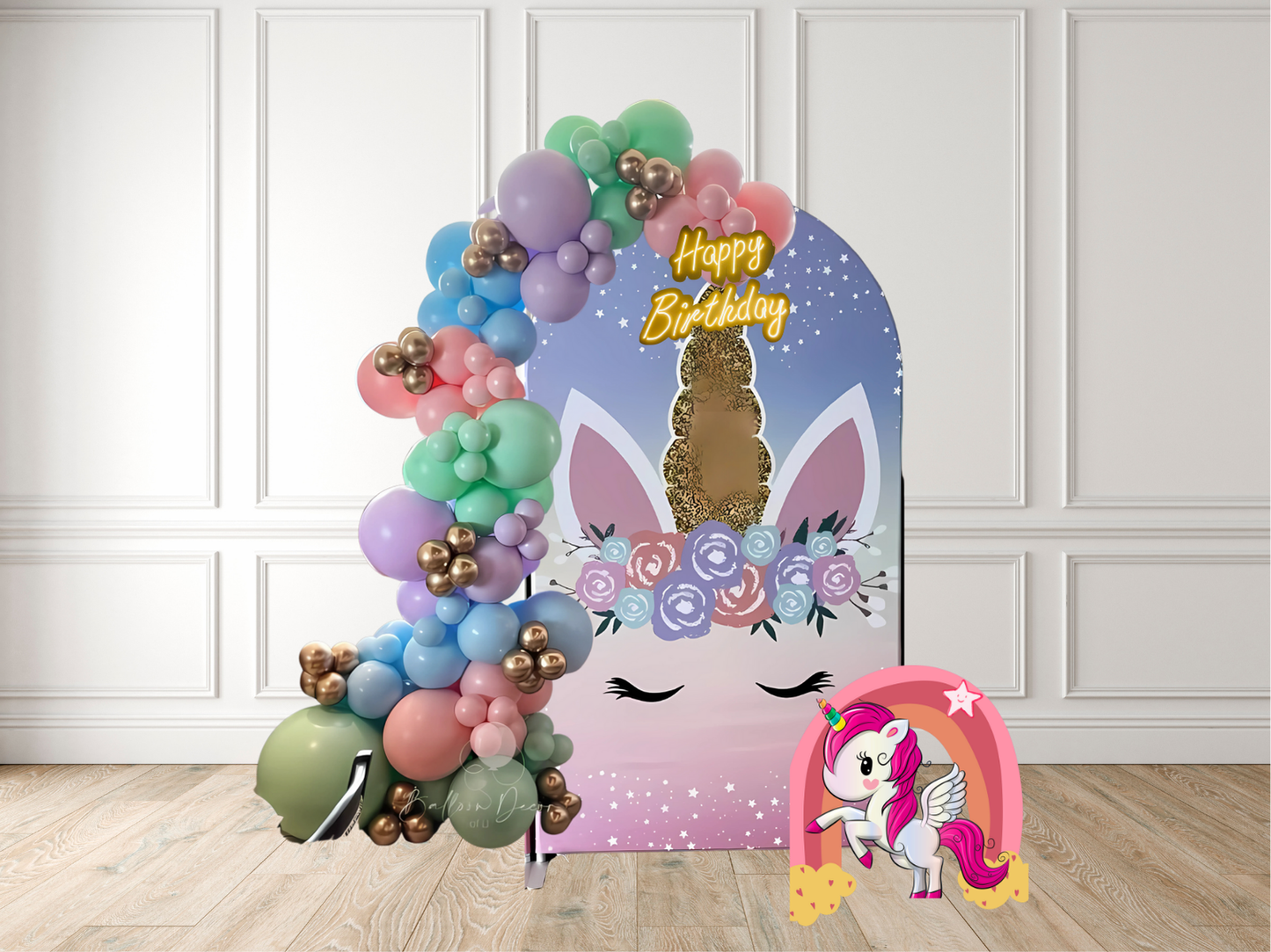 Birthday balloon arch with colorful balloons and a unicorn design on a wooden floor.