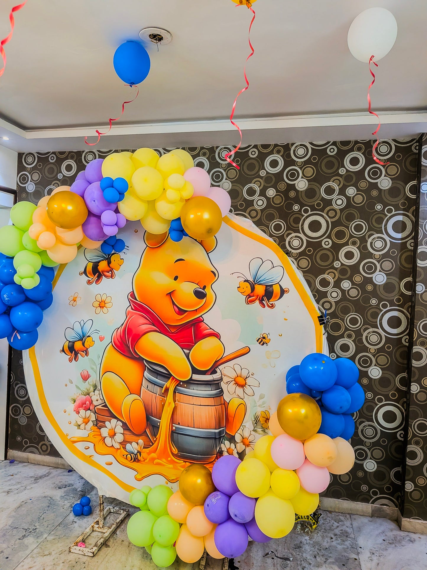 Decorative arch with balloons and Winnie the Pooh design on a wall.