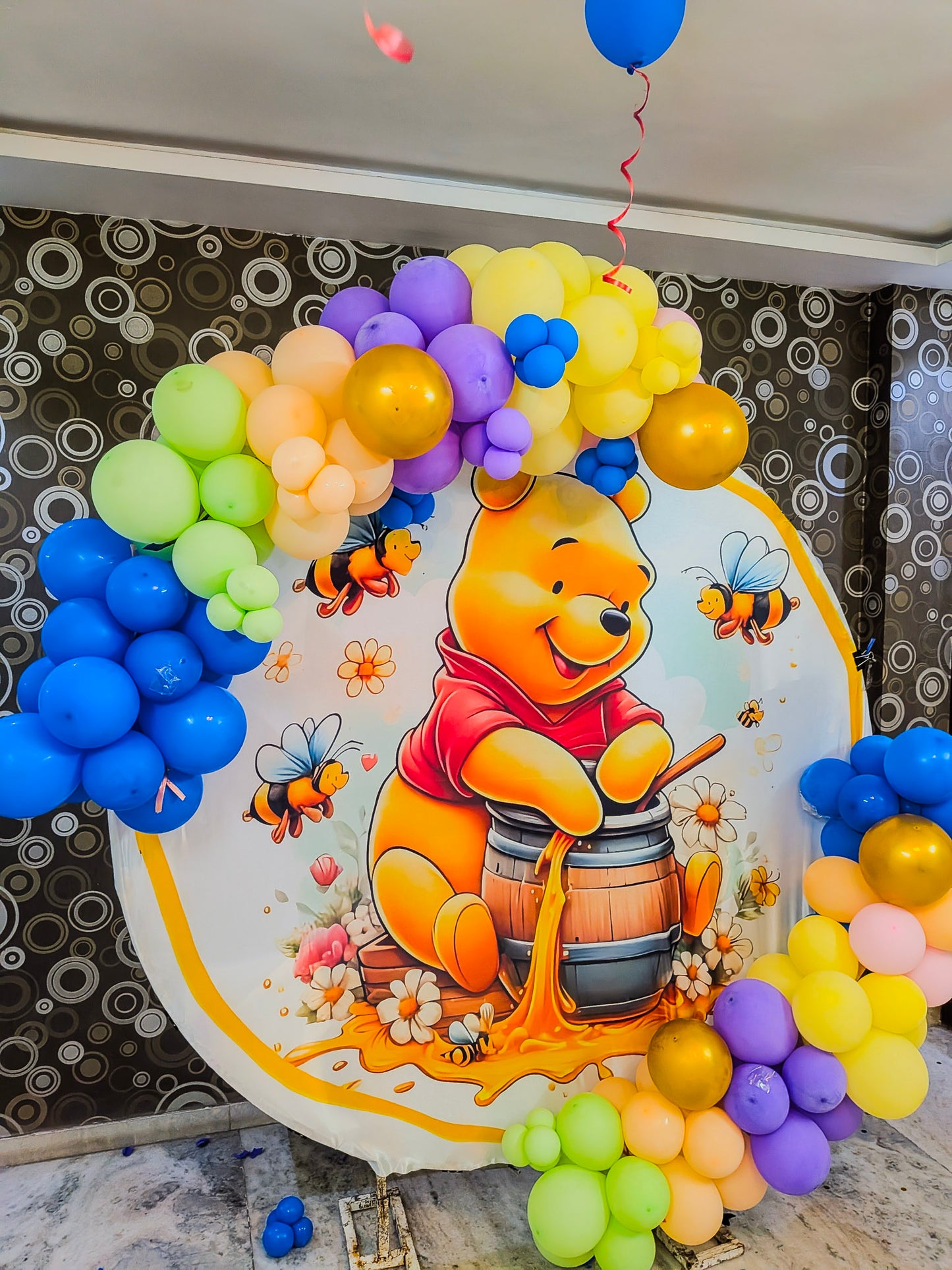 Decorative arch with balloons and a Winnie the Pooh poster on a patterned wall.