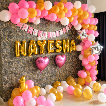 Decorative arch with balloons and 'Happy Birthday Nayesha' banner on a textured wall.