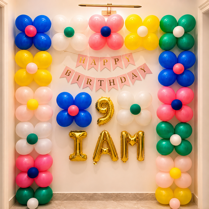 Colorful balloon decorations with 'Happy Birthday' banner and '9 I AM' gold balloons on a wall.