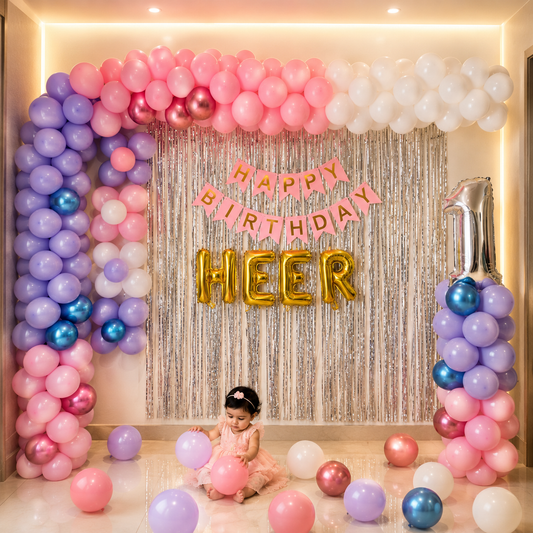 Child sitting among pink, purple, and white balloons with 'Happy Birthday Heer' banner.