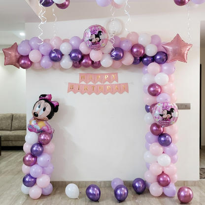 Balloon arch with Minnie Mouse decorations and 'Happy Birthday' banner in a room.