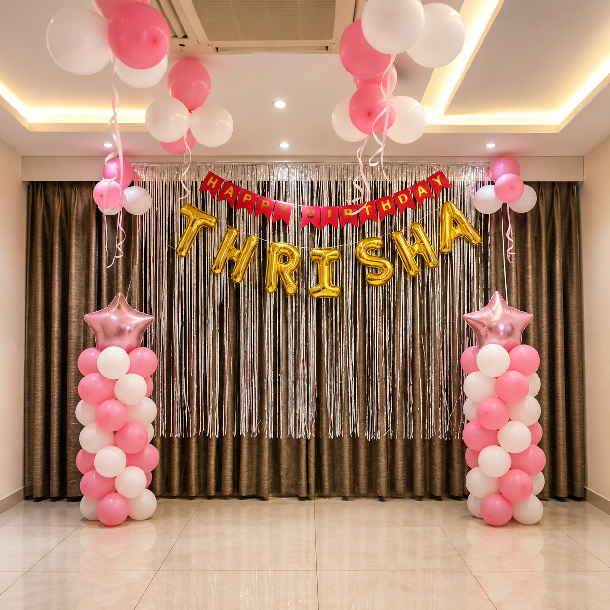 Decorative setup with balloons and 'Happy Birthday Thrisha' banner in a room.