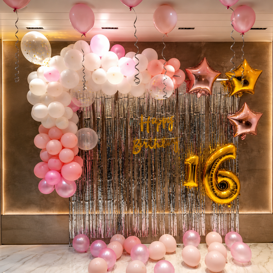 Decorative setup with balloons and 'Happy Birthday 16' banner on a metallic backdrop