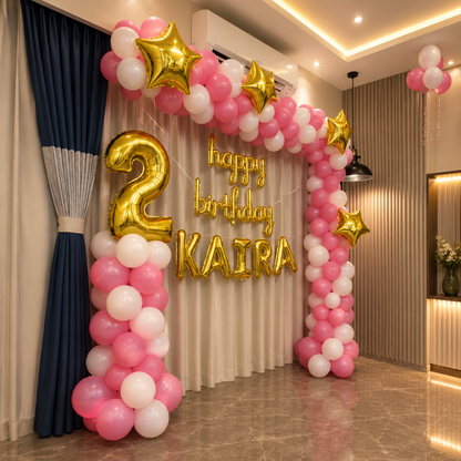 Birthday balloon arch with gold number 2 and 'happy birthday KAIRA' text in a room.