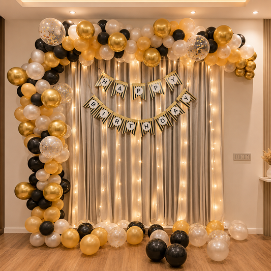 Birthday balloon arch with gold, black, and white balloons and a 'Happy Birthday' banner against a curtain backdrop.