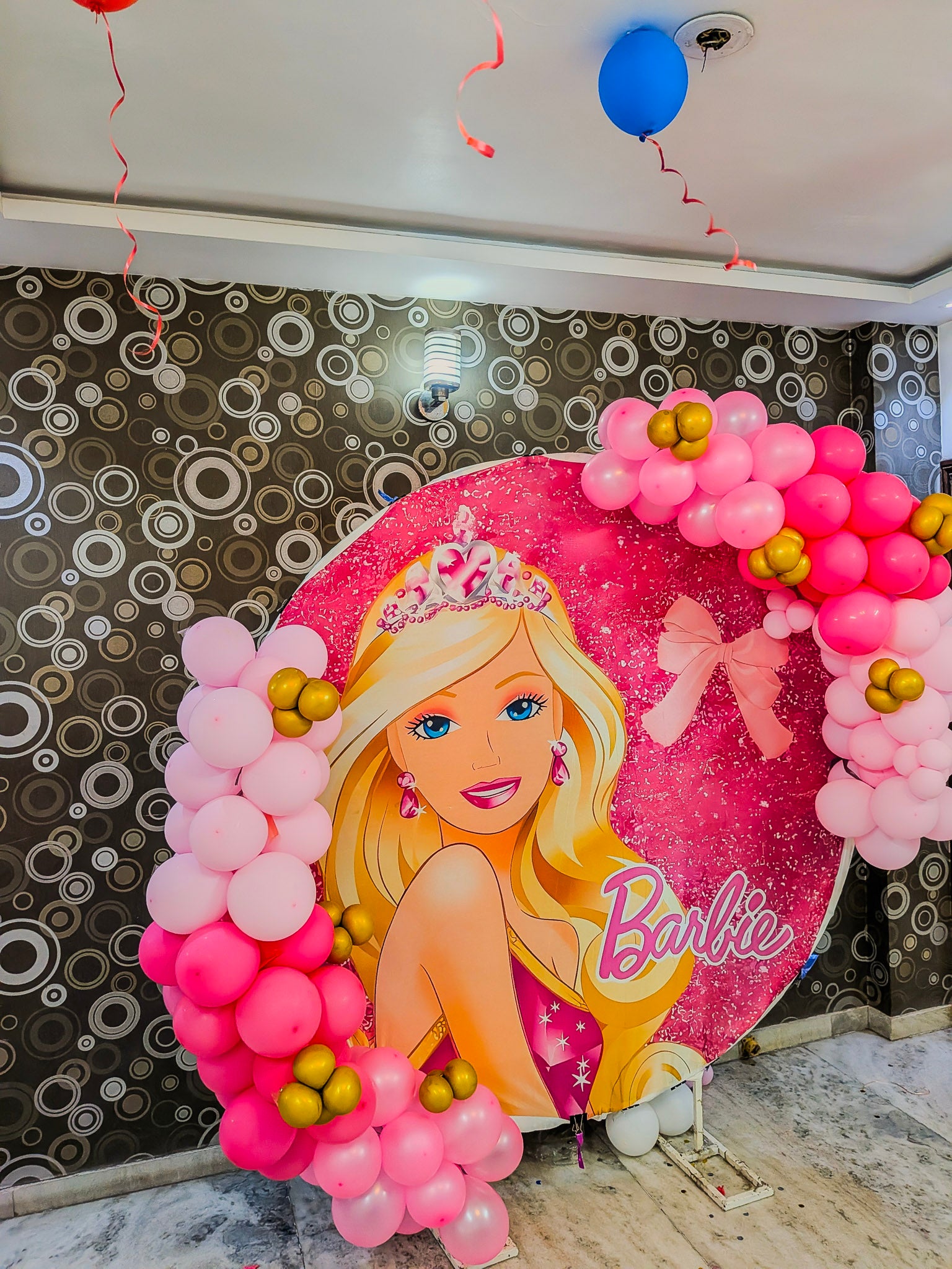 Barbie-themed balloon arch with pink and gold balloons against a decorative wall.