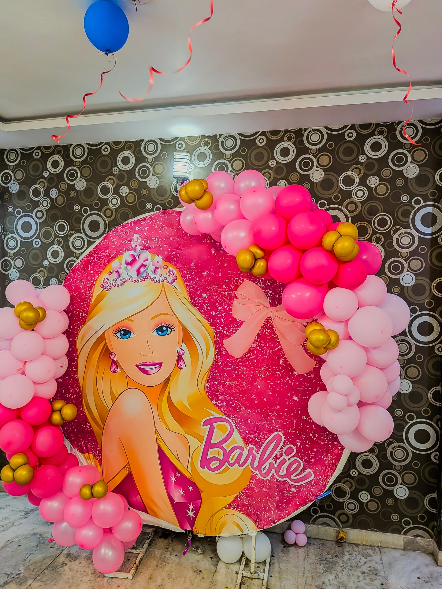Decorative arch with pink balloons and a Barbie-themed poster on a patterned wall.