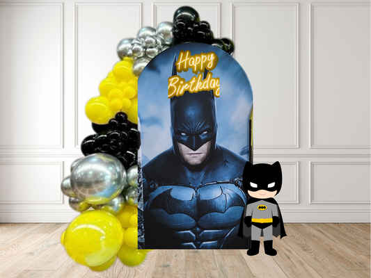 Batman-themed birthday banner with balloons and a small Batman figure on a wooden floor.