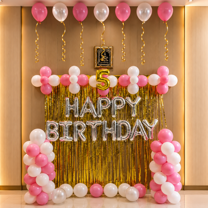 Birthday decoration with balloons and 'Happy Birthday' banner on a wall.