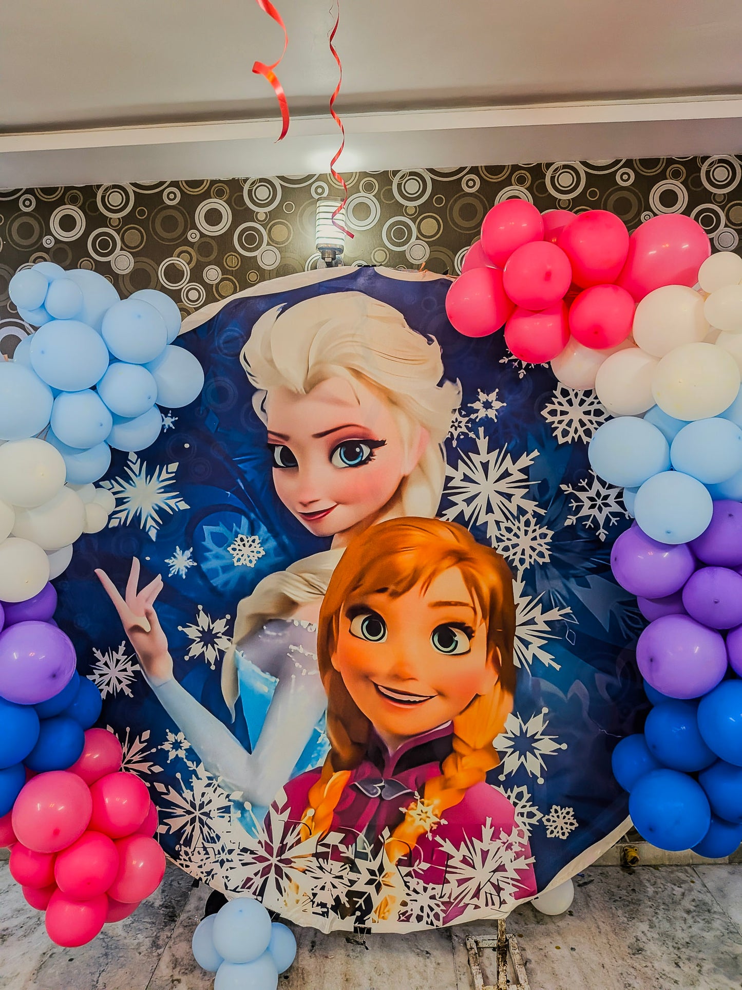 Decorative backdrop with Elsa and Anna from Frozen surrounded by colorful balloons.