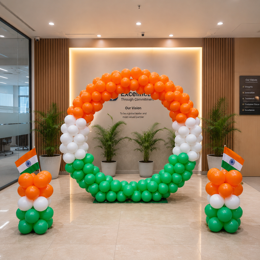 A large balloon arch decoration in the shape of a circle, decorated with orange, white, and green balloons in the colors of the Indian flag, set in a modern office lobby. Two smaller matching balloon arrangements with Indian flags are placed on either side of the arch.