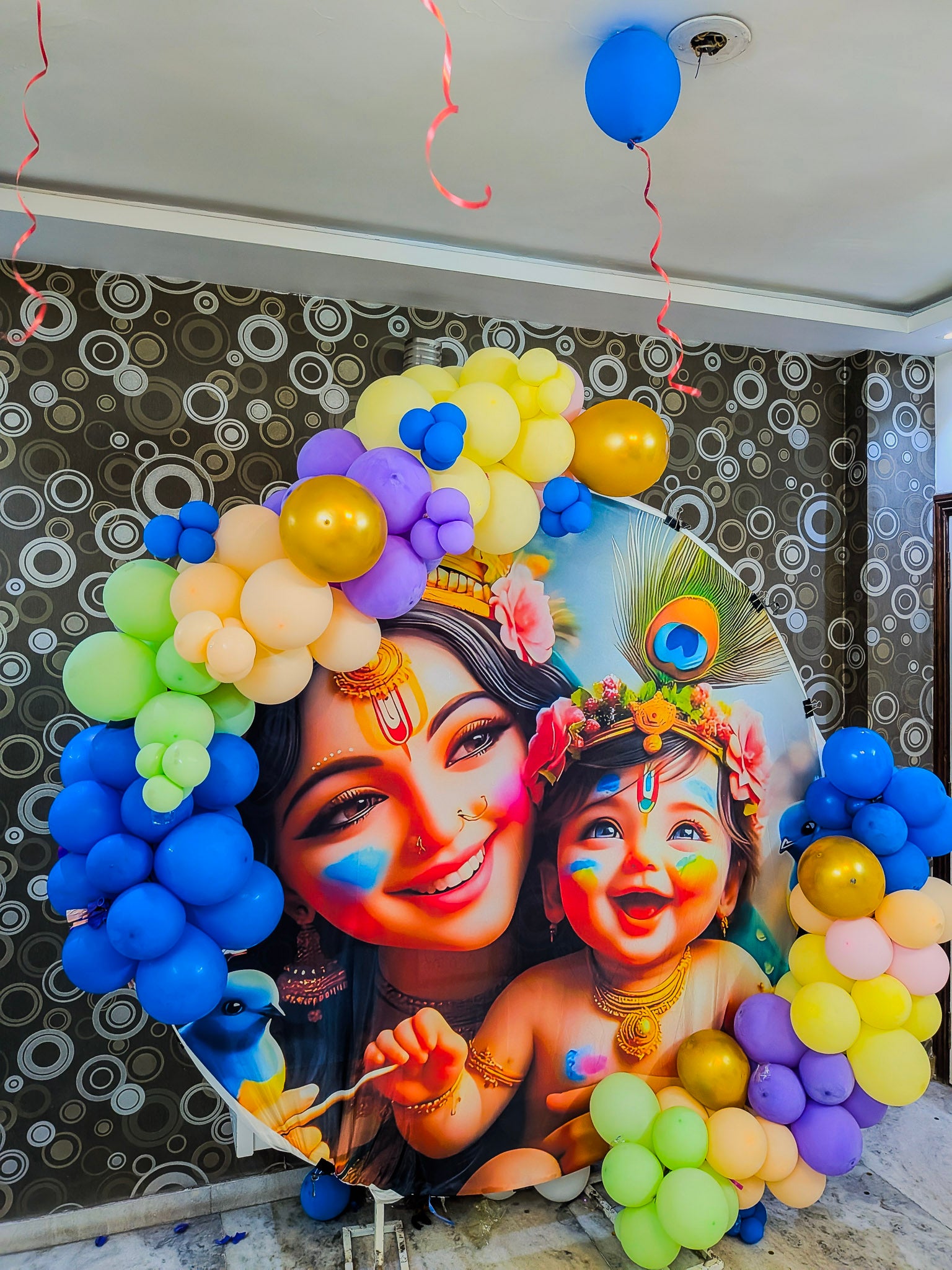 Decorative setup with balloons and a portrait of a woman and child against a patterned wall.