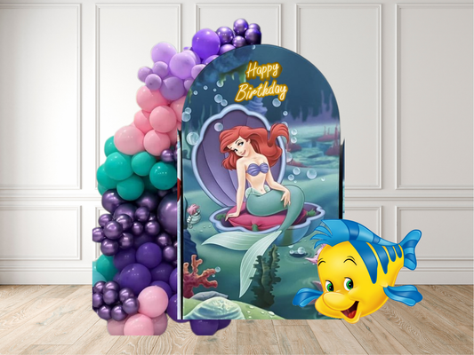 Mermaid-themed birthday party setup with balloons and decorations on a wooden floor.