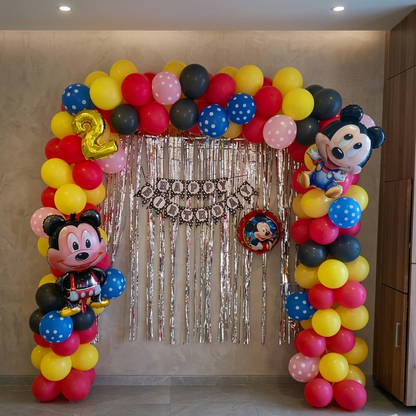 Balloon arch with Mickey Mouse decorations and '2' balloon in a room.