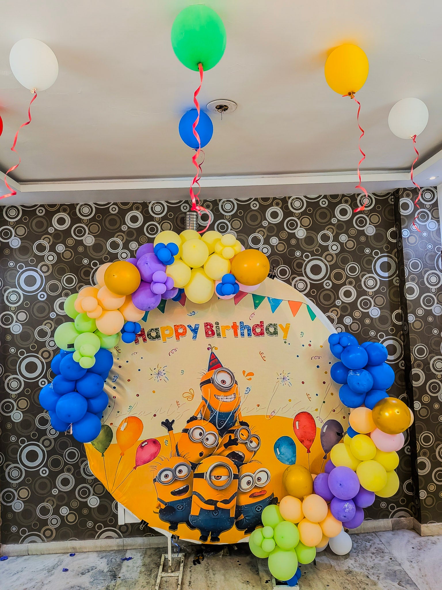 Birthday decoration with balloons and a Minions-themed balloon in front of a patterned wall.