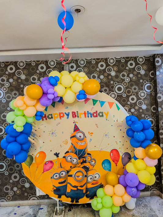 Birthday balloon arch with Minions design and 'Happy Birthday' text on a patterned wall.