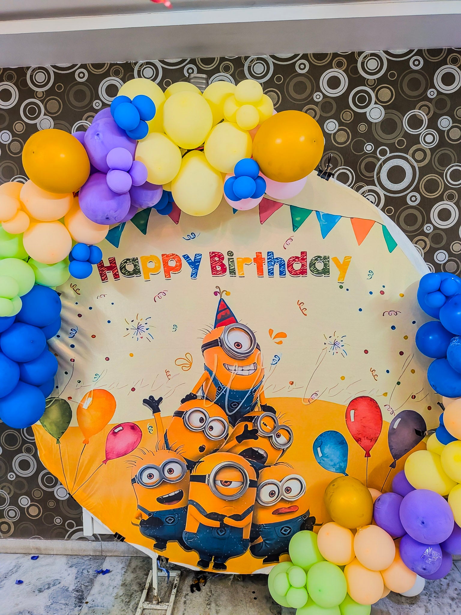 Birthday balloon arch with Minions design and 'Happy Birthday' text against a patterned background.