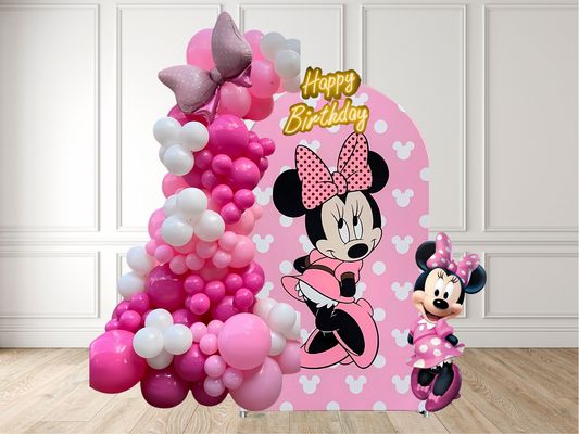 Minnie Mouse-themed birthday balloon arch with a small Minnie Mouse figure on a wooden floor.