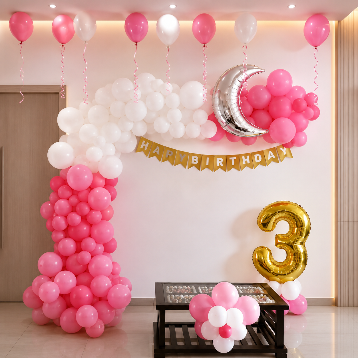 Pink and white balloon arch with 'Happy Birthday' banner and number '3' balloon in a room.