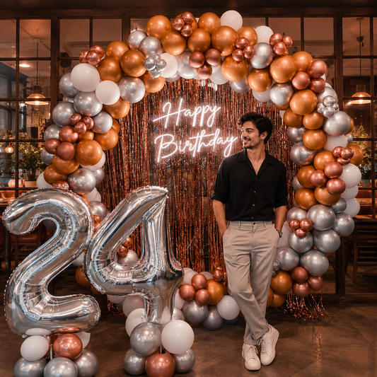 Man standing in front of a 'Happy Birthday' arch with balloons and number 24 in a decorated room.