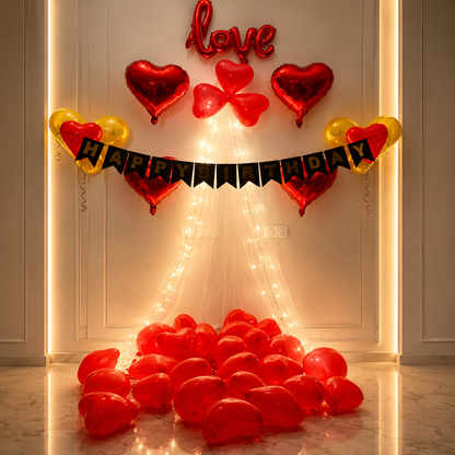 Decorative setup with heart-shaped balloons, 'love' balloon, and 'Happy Birthday' banner on a light-colored wall.