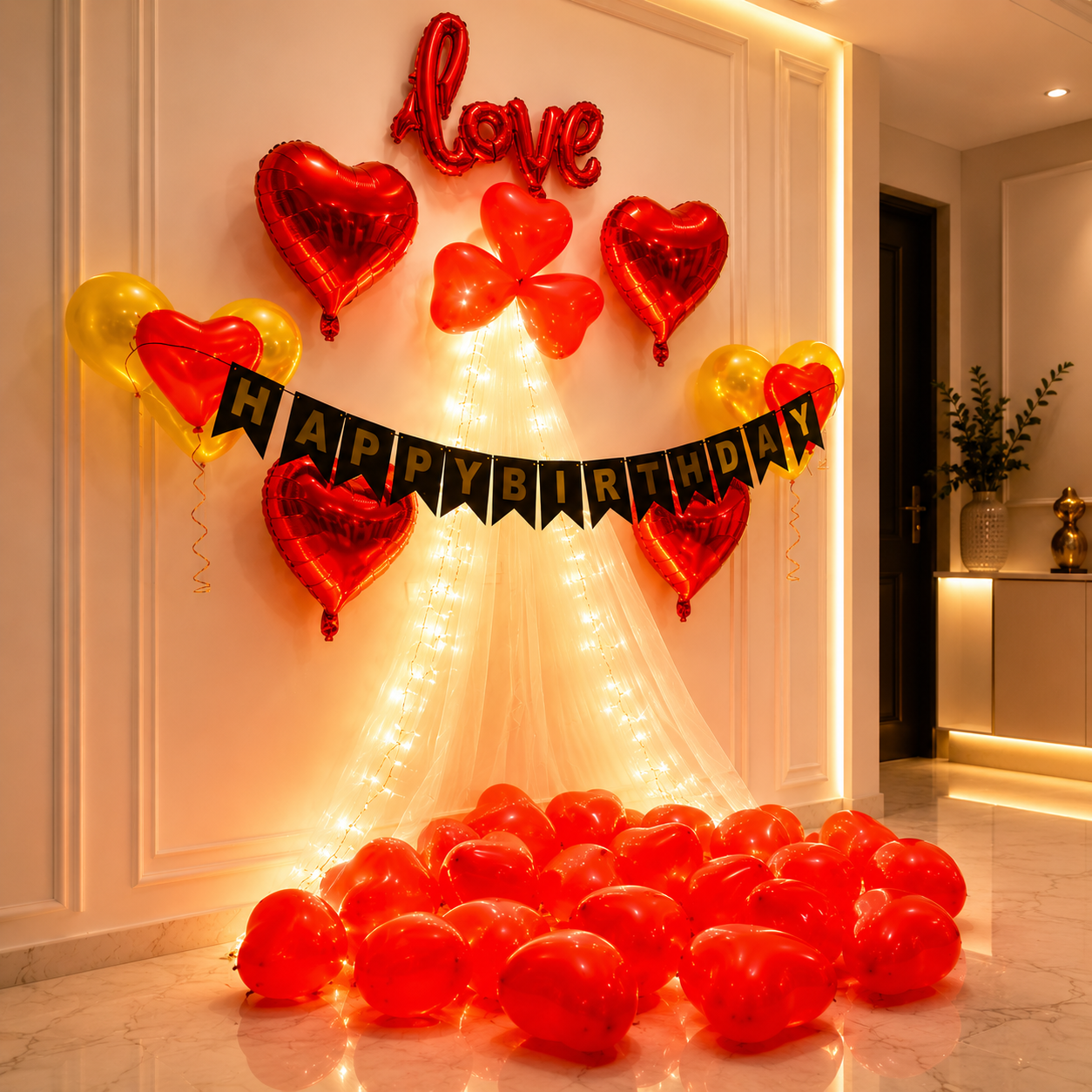 Decorative setup with red heart-shaped balloons, 'Love' and 'Happy Birthday' text, and string lights on a wall.