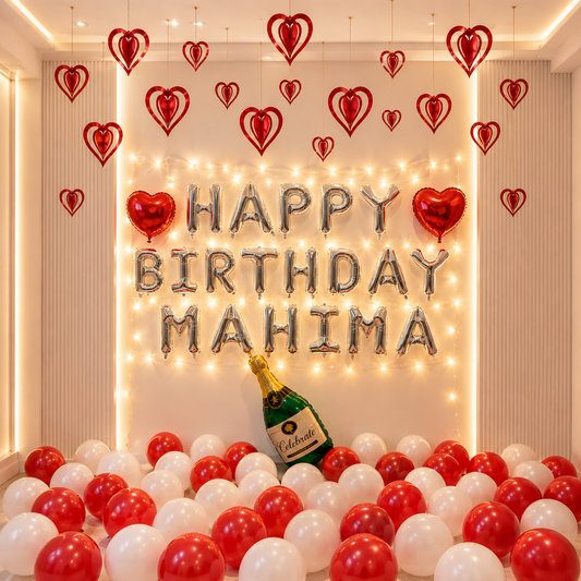 Birthday decoration with 'Happy Birthday Mahima' balloons, red and white balloons, and a bottle of champagne.
