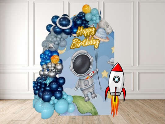 Space-themed birthday balloon arch with astronaut, rocket, and planets against a white wall.