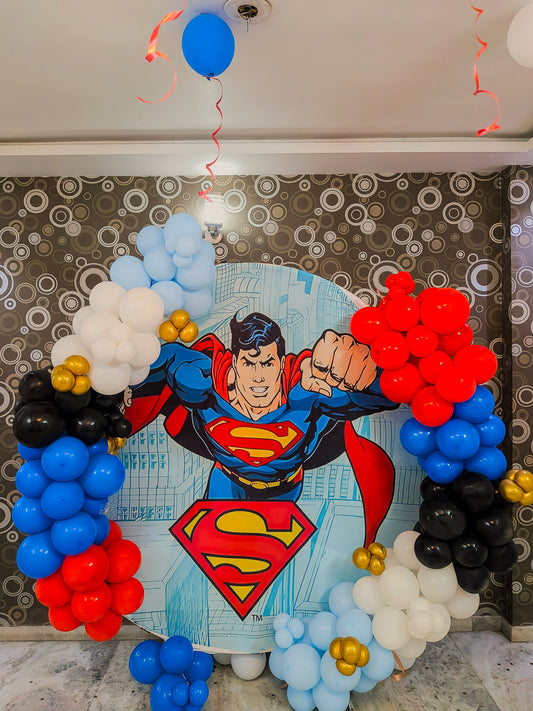 Superman-themed balloon arch with colorful balloons against a patterned wall.