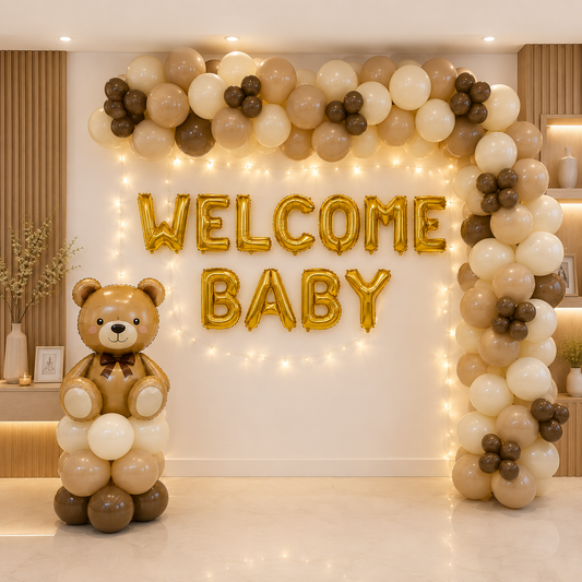 Decorative setup with balloons, a teddy bear, and 'Welcome Baby' text in a room.