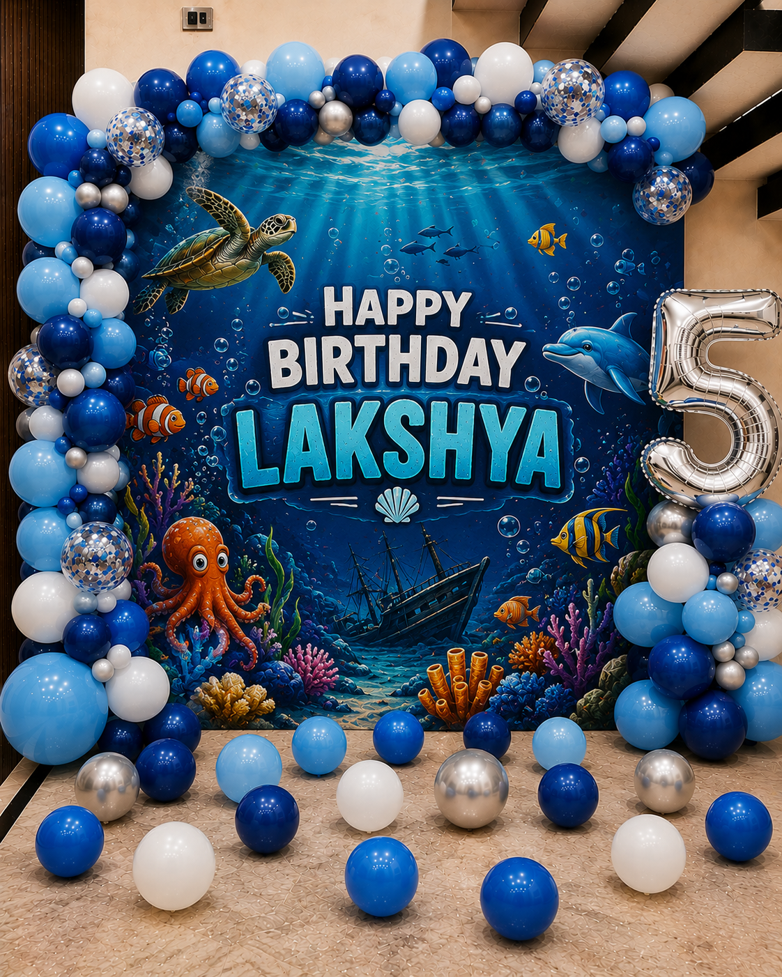 Underwater-themed birthday decoration with balloons and 'Happy Birthday Lakshya' sign.