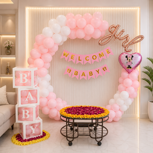 Baby shower setup with pink and white balloon arch, 'Welcome Baby Girl' banner, and decorative elements.